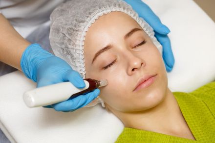 Cosmetic facial treatment with a handheld device applied to a woman wearing a hair cap and blue gloves