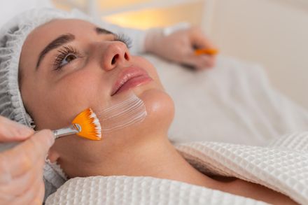Woman receiving a facial treatment with orange brush on her chin in a spa setting