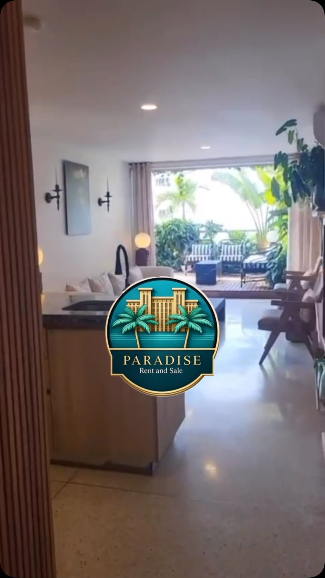 Luminoso salón con sofá, lámparas, plantas y vistas abiertas a un patio tropical.