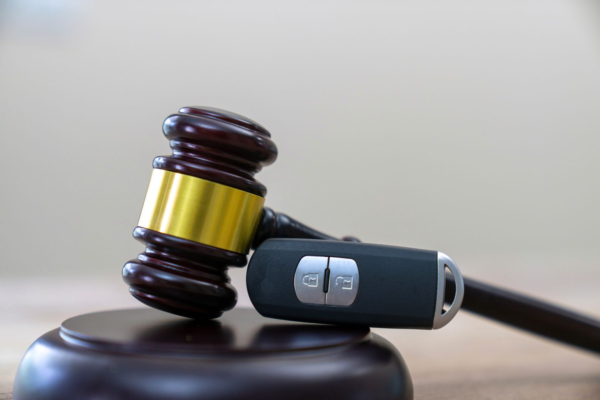 A wooden gavel rests atop a car key on a wooden block, suggesting a vehicle auction or legal matter.