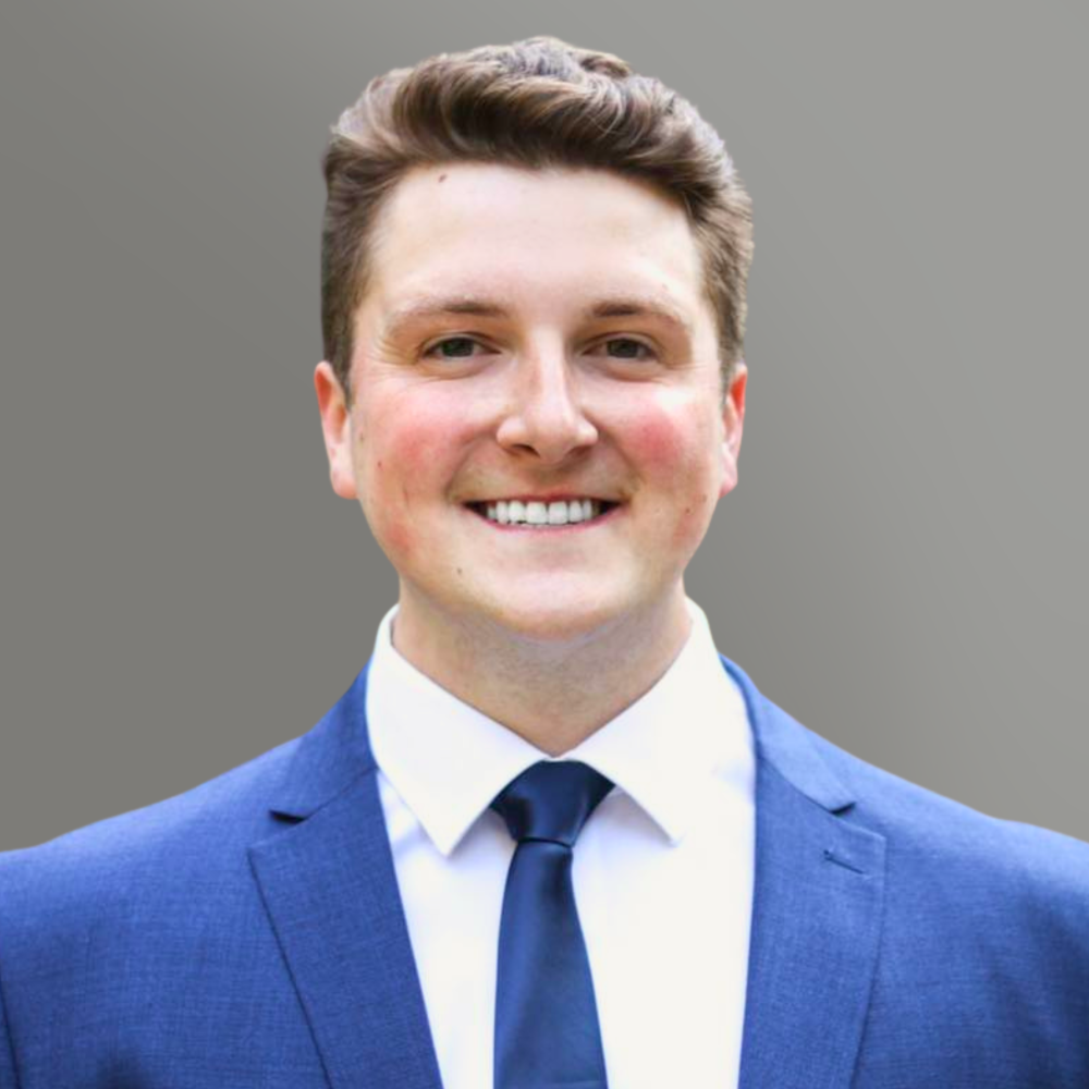 Smiling person in a blue suit and tie against a neutral gray background