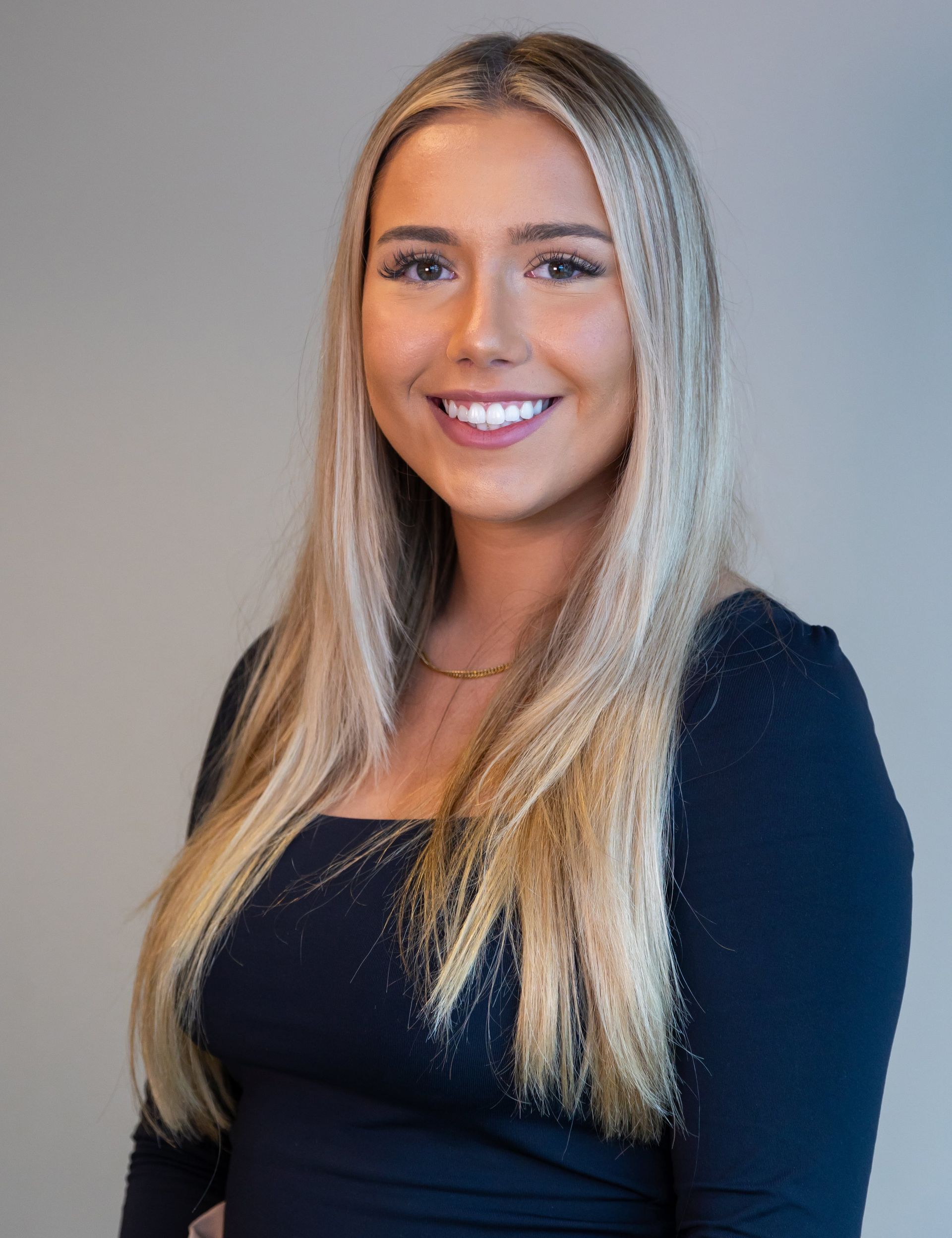 Smiling blonde woman in a dark top against a gray background