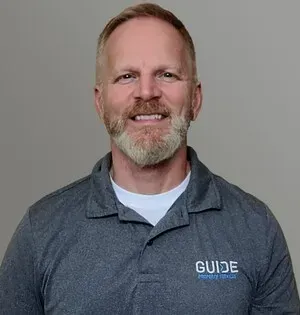 Smiling person in a gray GUIDE polo shirt against a plain gray background