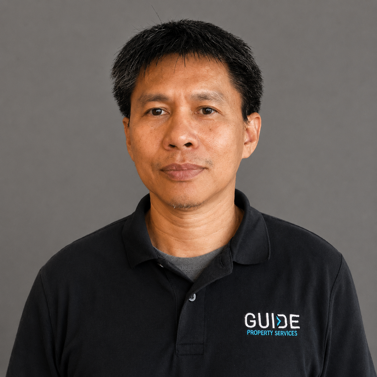 Person in a dark navy polo shirt with a GUIDE logo, standing against a plain gray background.