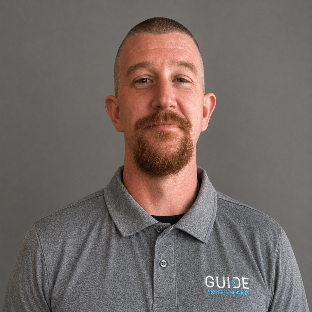 Man in a gray polo shirt with a GUIDE logo, standing against a plain gray background.