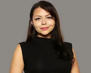 Woman in a black sleeveless top smiling against a plain gray background