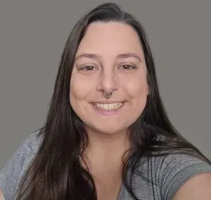 Smiling person with long dark hair and a gray shirt against a plain gray background