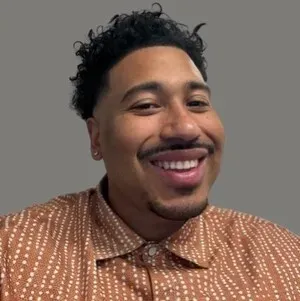 Smiling person in a brown patterned shirt against a gray background