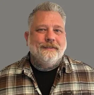 Smiling bearded man in a plaid shirt against a gray background