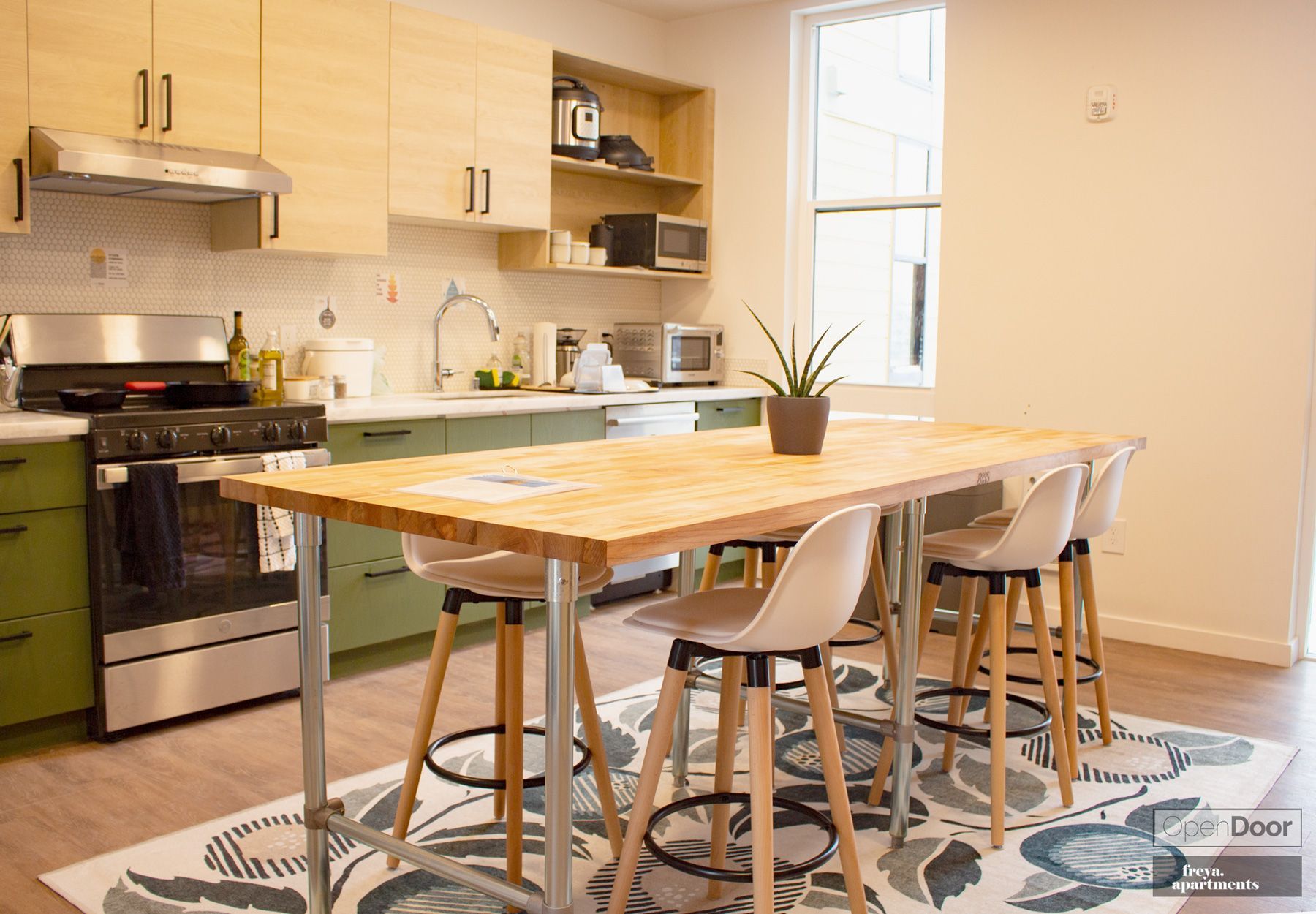 Bright modern kitchen with a wooden island, stools, stove, shelves, and patterned rug