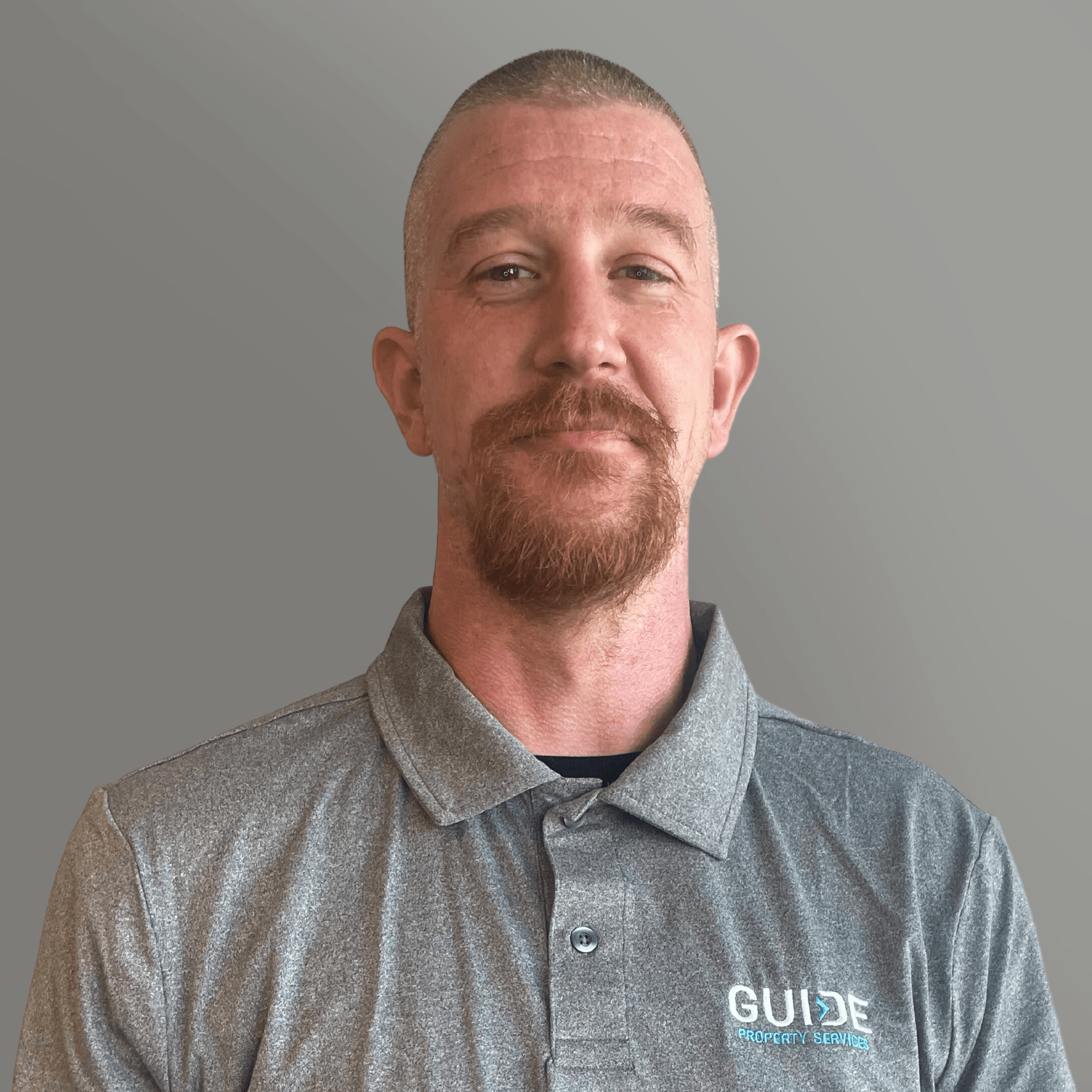Man in a gray polo shirt with a GUIDE logo, standing against a plain gray background.