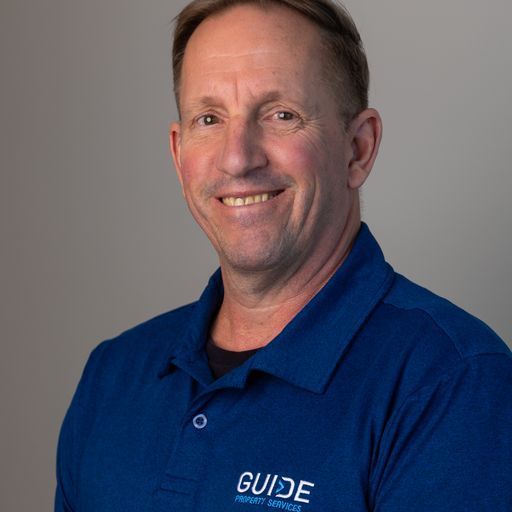 Smiling person in a blue GUIDE polo shirt against a plain gray background