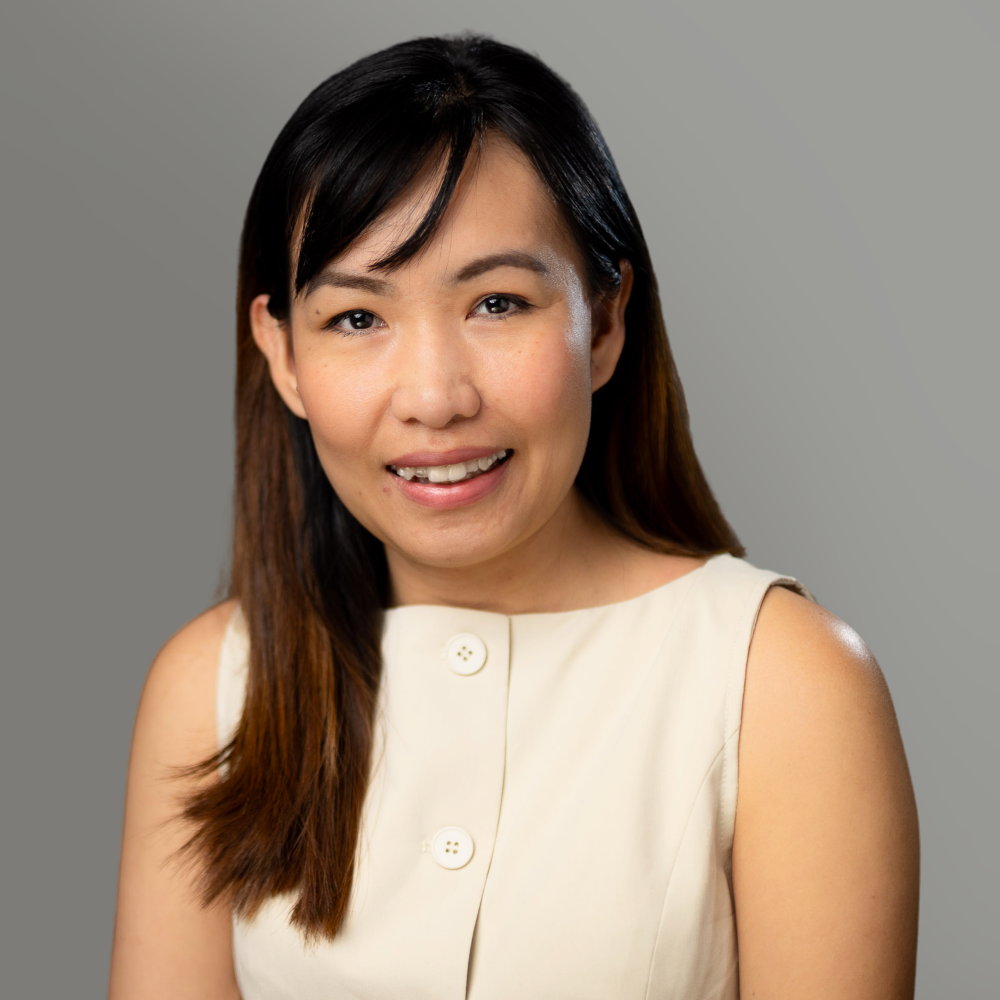 Smiling woman in a cream sleeveless top against a gray background