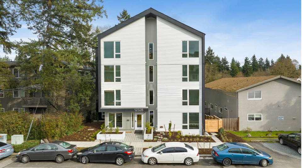 Modern four-story apartment building with parked cars in front and trees around it