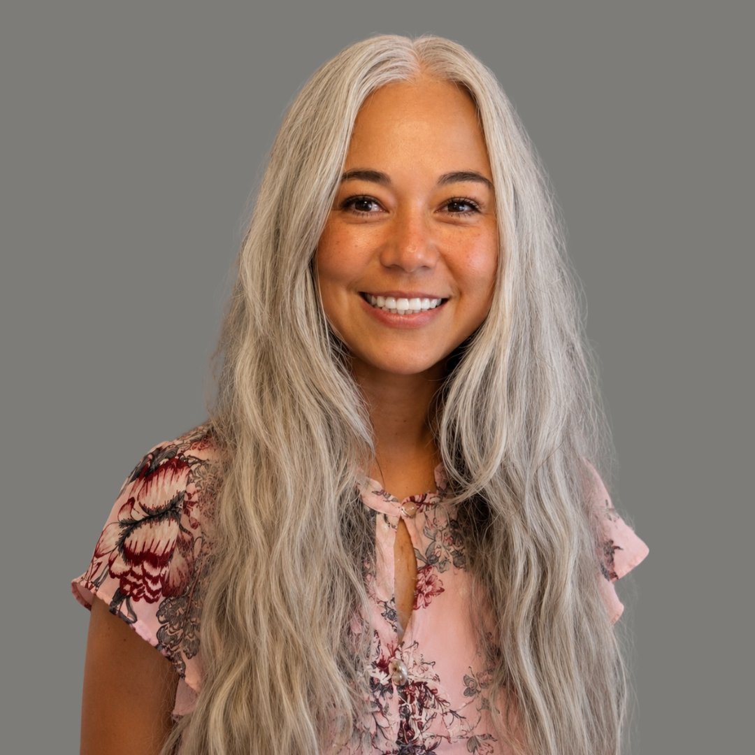 Smiling woman with long blonde hair in a gray blazer against a light background