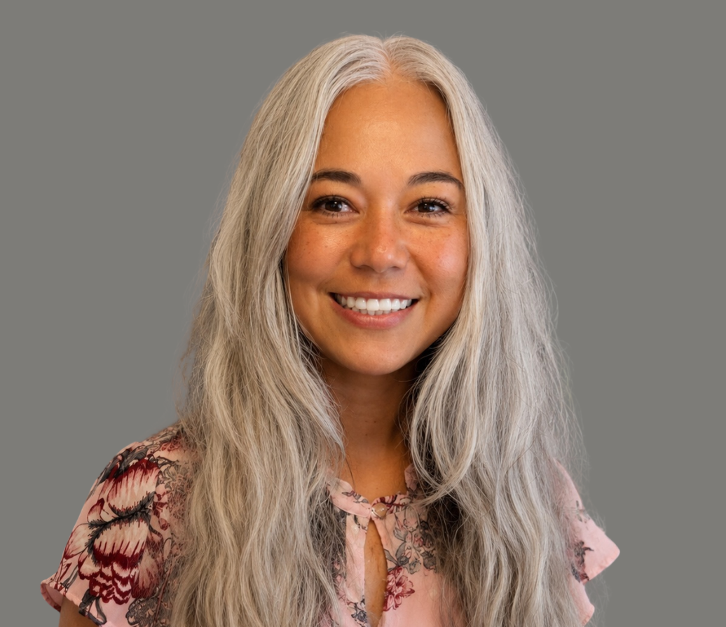 Smiling woman with long blonde hair in a gray blazer against a light background
