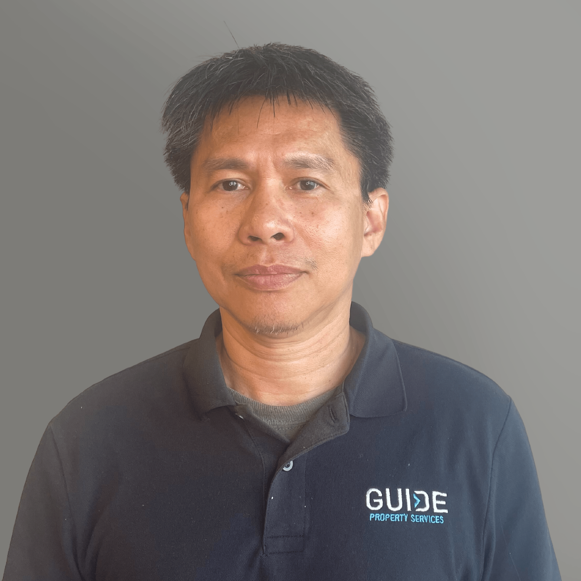 Person in a dark navy polo shirt with a GUIDE logo, standing against a plain gray background.