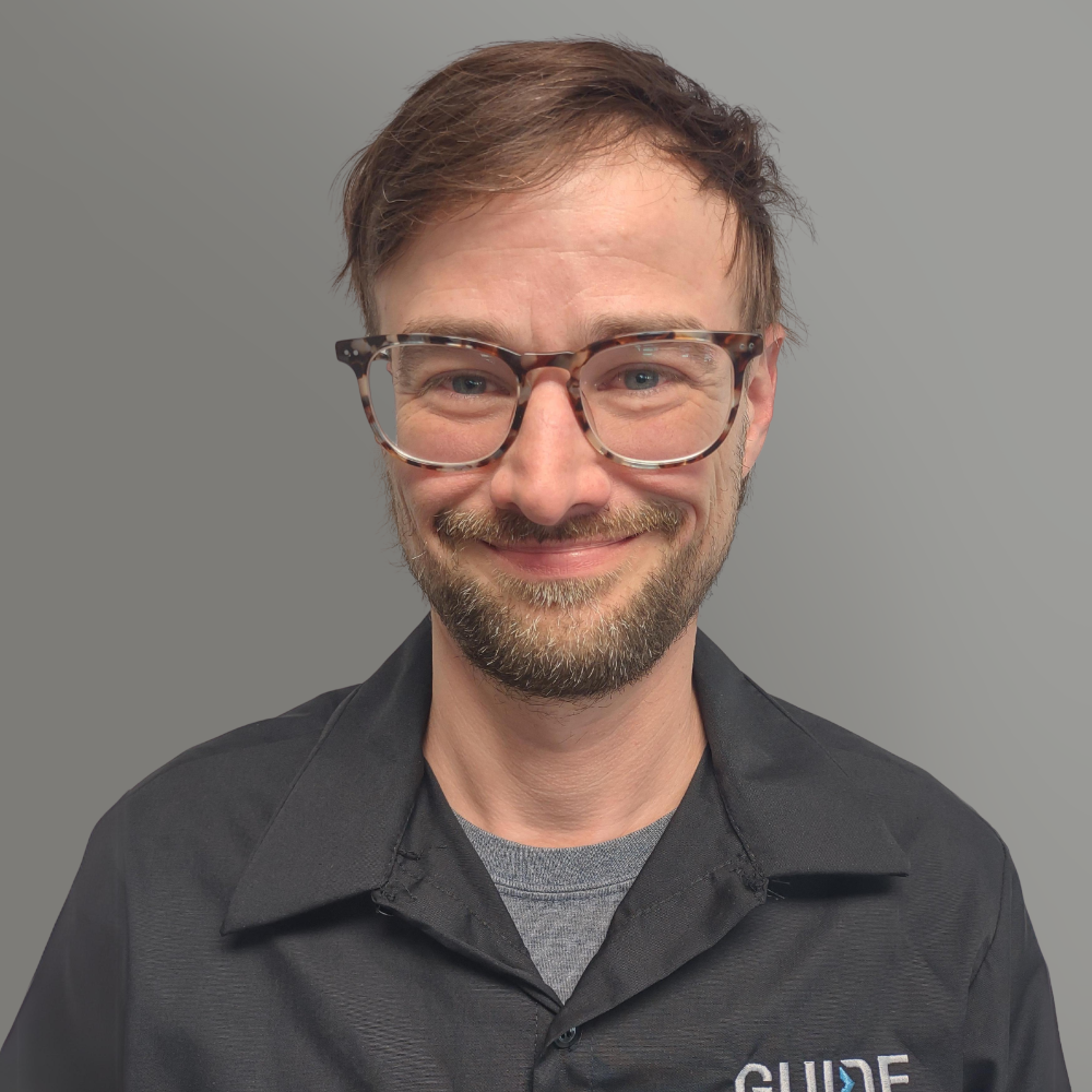 Portrait of a smiling person wearing glasses and a dark jacket against a gray background