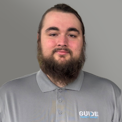 Man in gray polo shirt with GUIDE logo, facing camera against a plain gray background