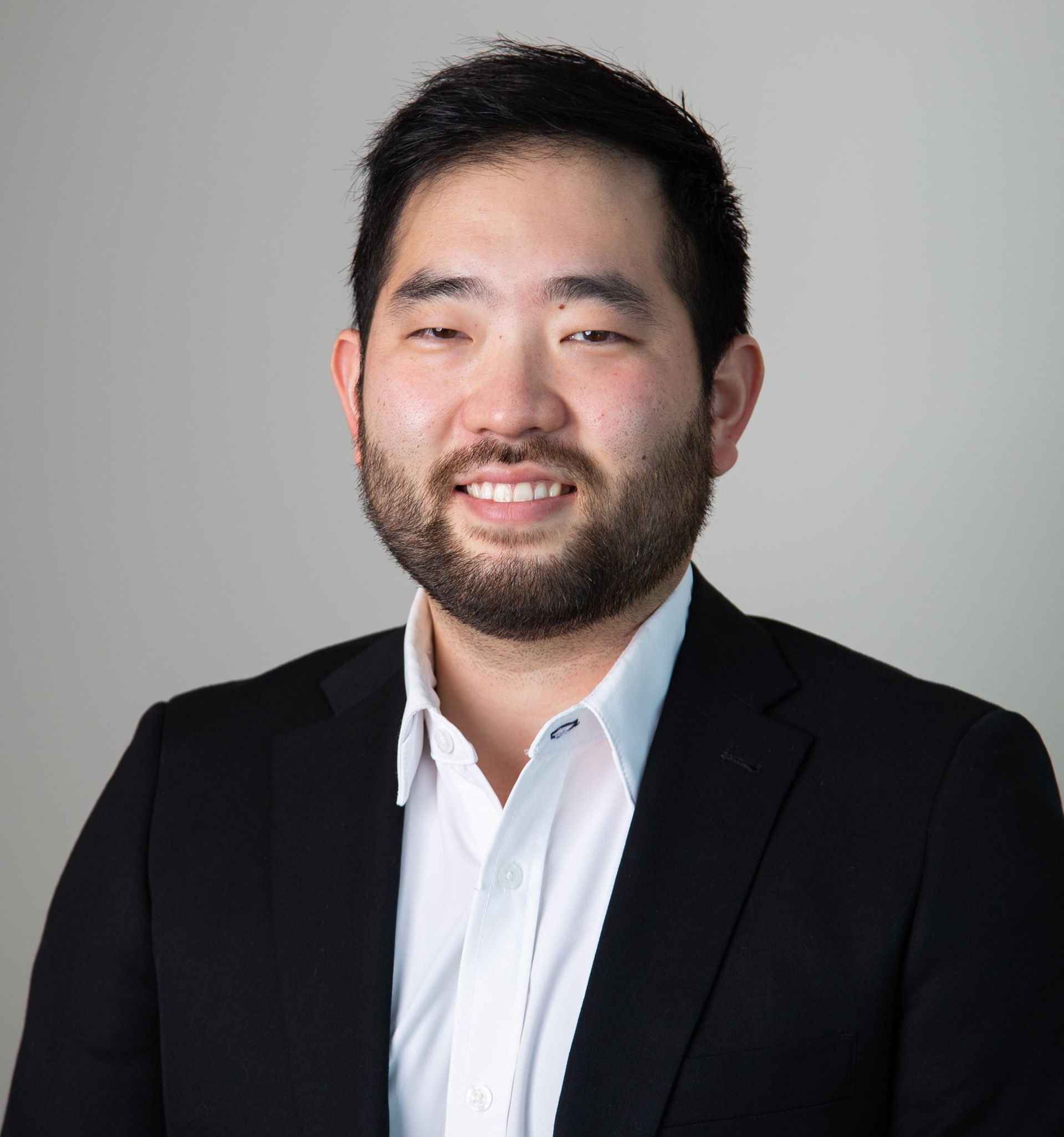 Portrait of a smiling person in a black blazer and white shirt against a gray background