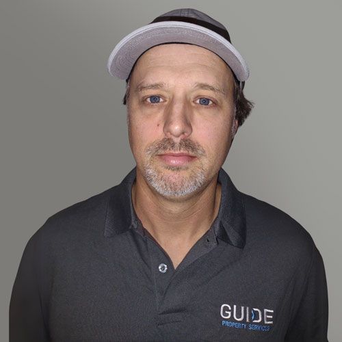 Man wearing a black visor and dark polo shirt with a “GUIDE” logo, facing forward against a gray background