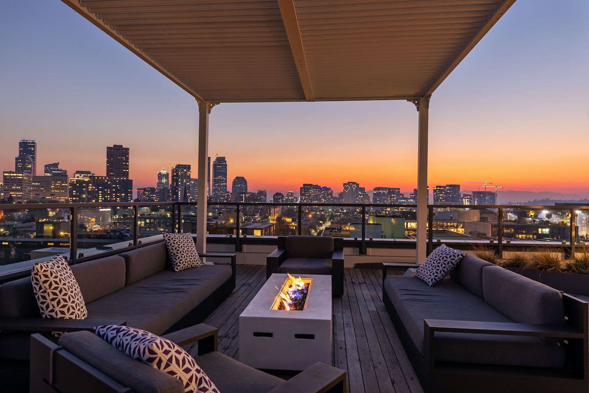 Rooftop lounge at sunset with city skyline and cushioned seating around a fire table