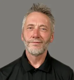 Portrait of a man in a black polo shirt against a gray background, with a slight smile.