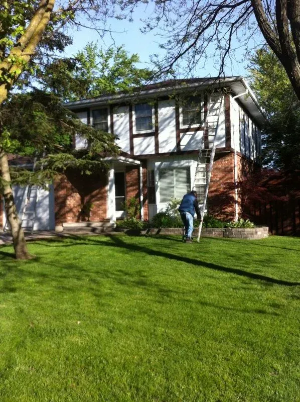 A man is standing in front of a house cutting a tree