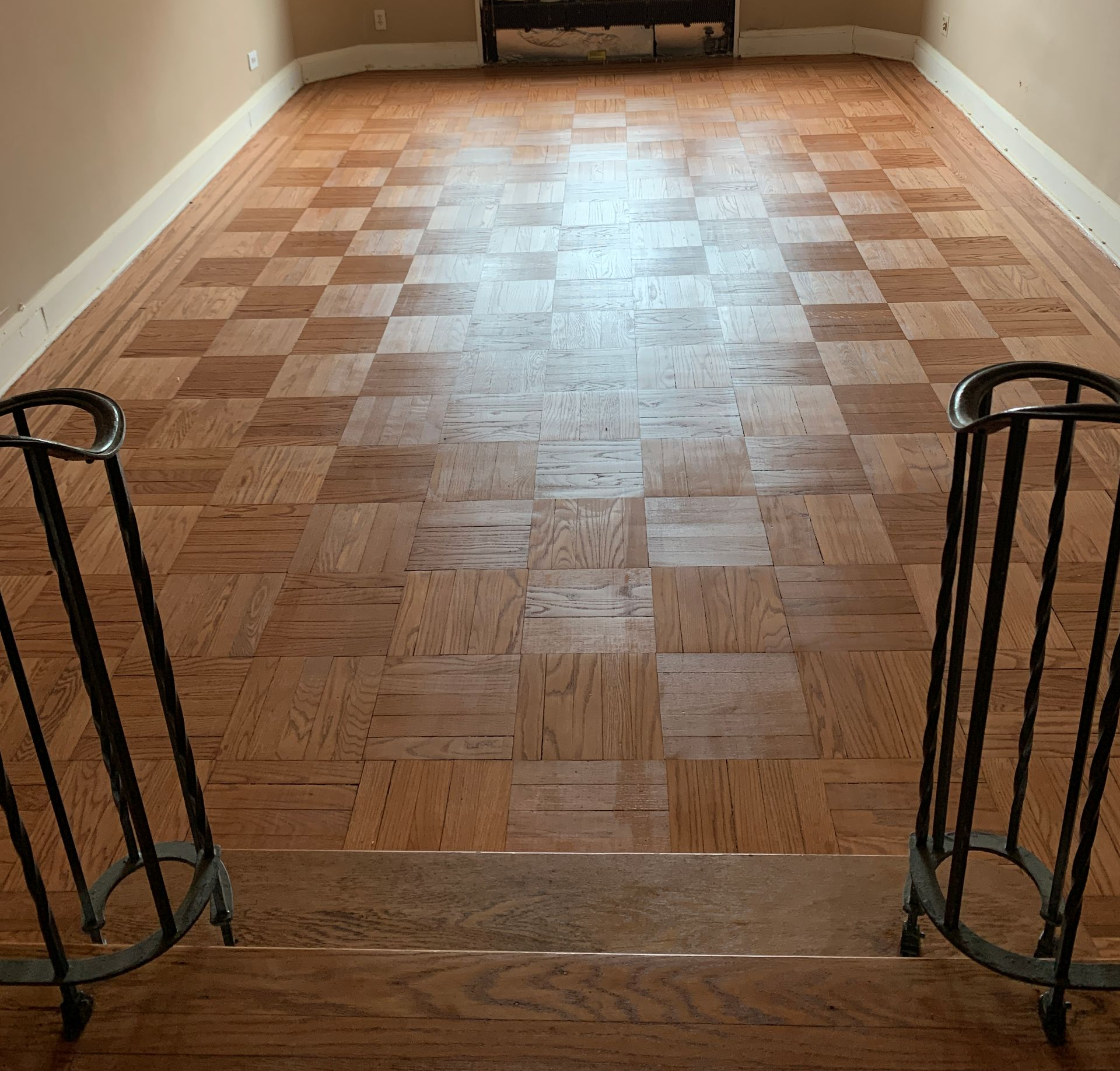 Shiny, dark brown hardwood floor reflecting light, with a portion of a staircase in the background.