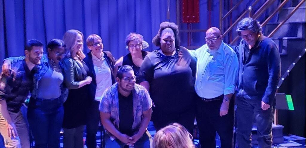 Group of people posing on a dim blue-lit stage with stairs and railings in the background