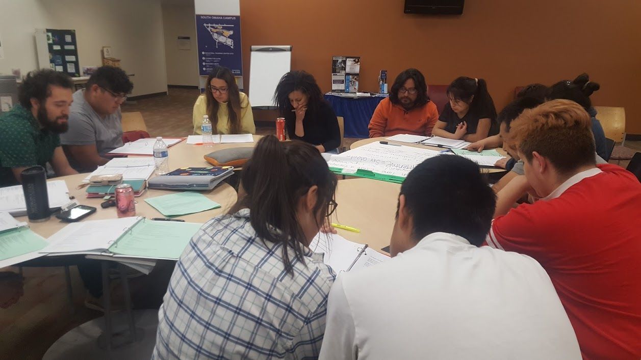 People gathered around tables in a meeting room, working together on large sheets of paper.