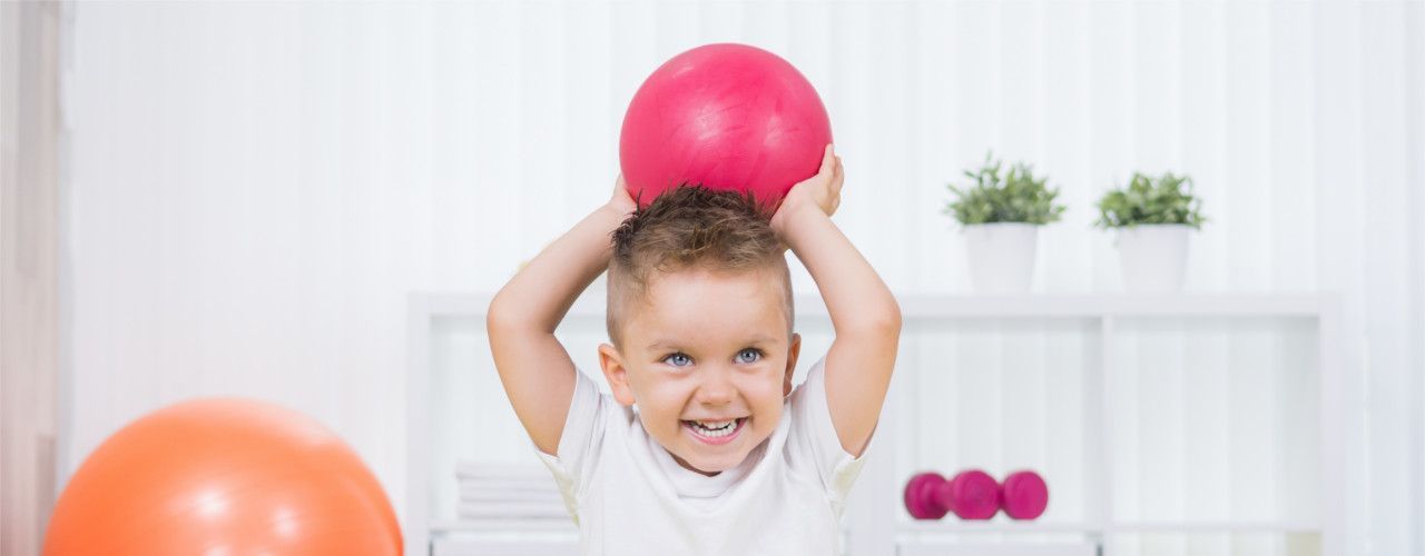 A little boy is holding a pink ball over his head.
