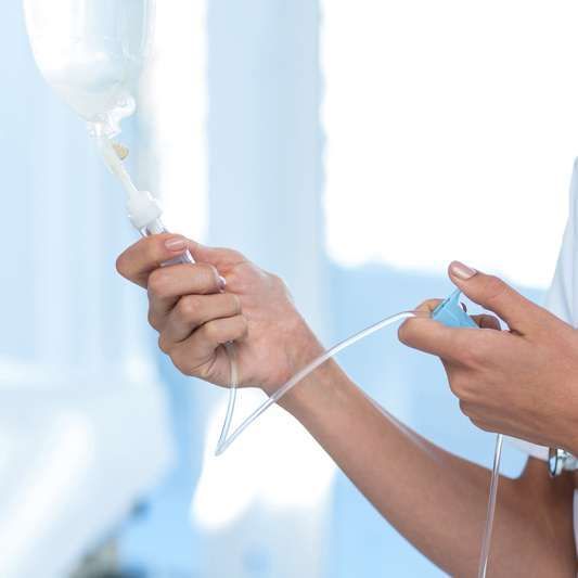 Nurse's hands adjusting an intravenous (IV) drip bag and tubing in a medical setting.