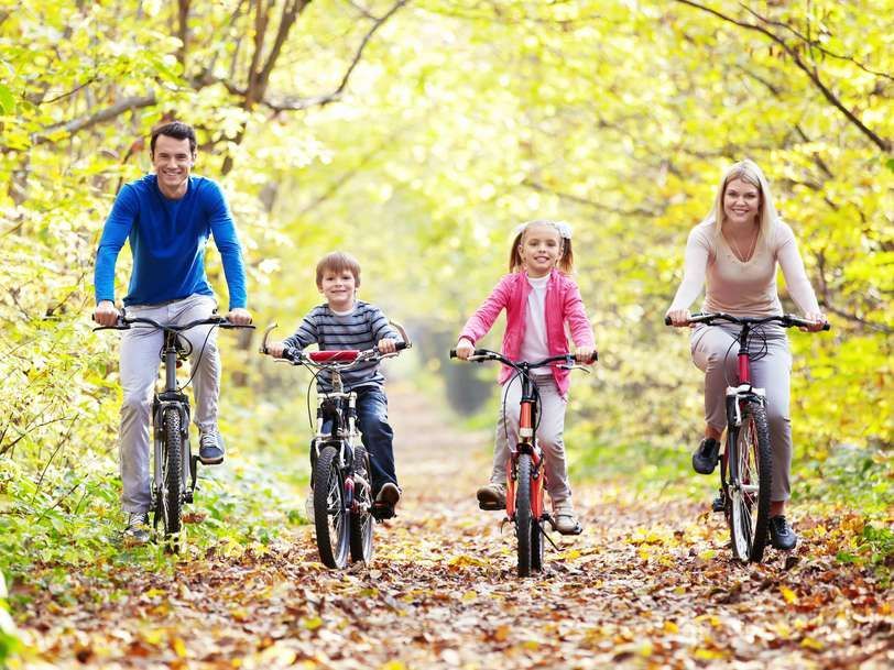 Family of four biking on a path through a wooded area with fall foliage.