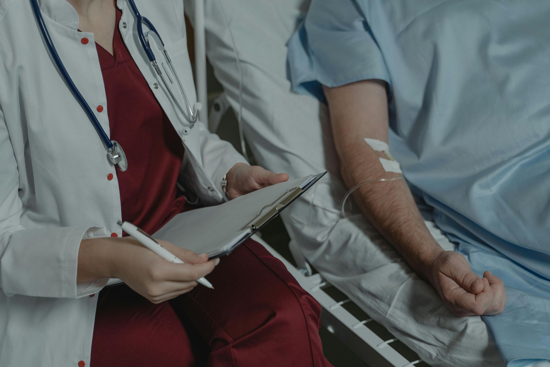 Doctor in white coat reviewing patient's chart, patient in bed with IV.