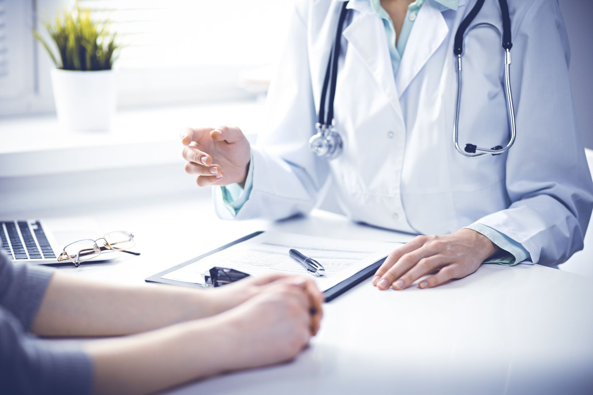 Doctor in white coat speaking with a patient at a desk in a bright clinic office