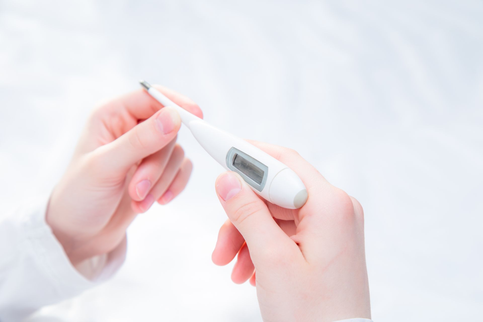 Hands holding a white digital thermometer against a white background.
