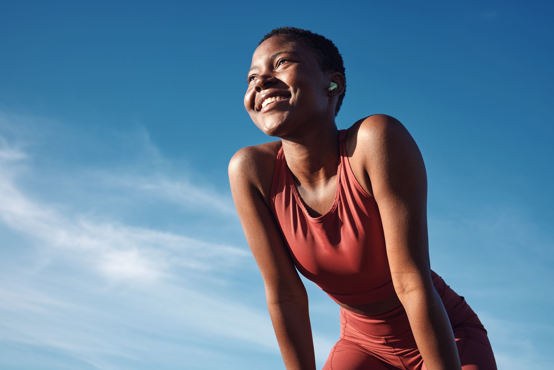 Smiling person in a red sleeveless top leaning forward under a bright blue sky