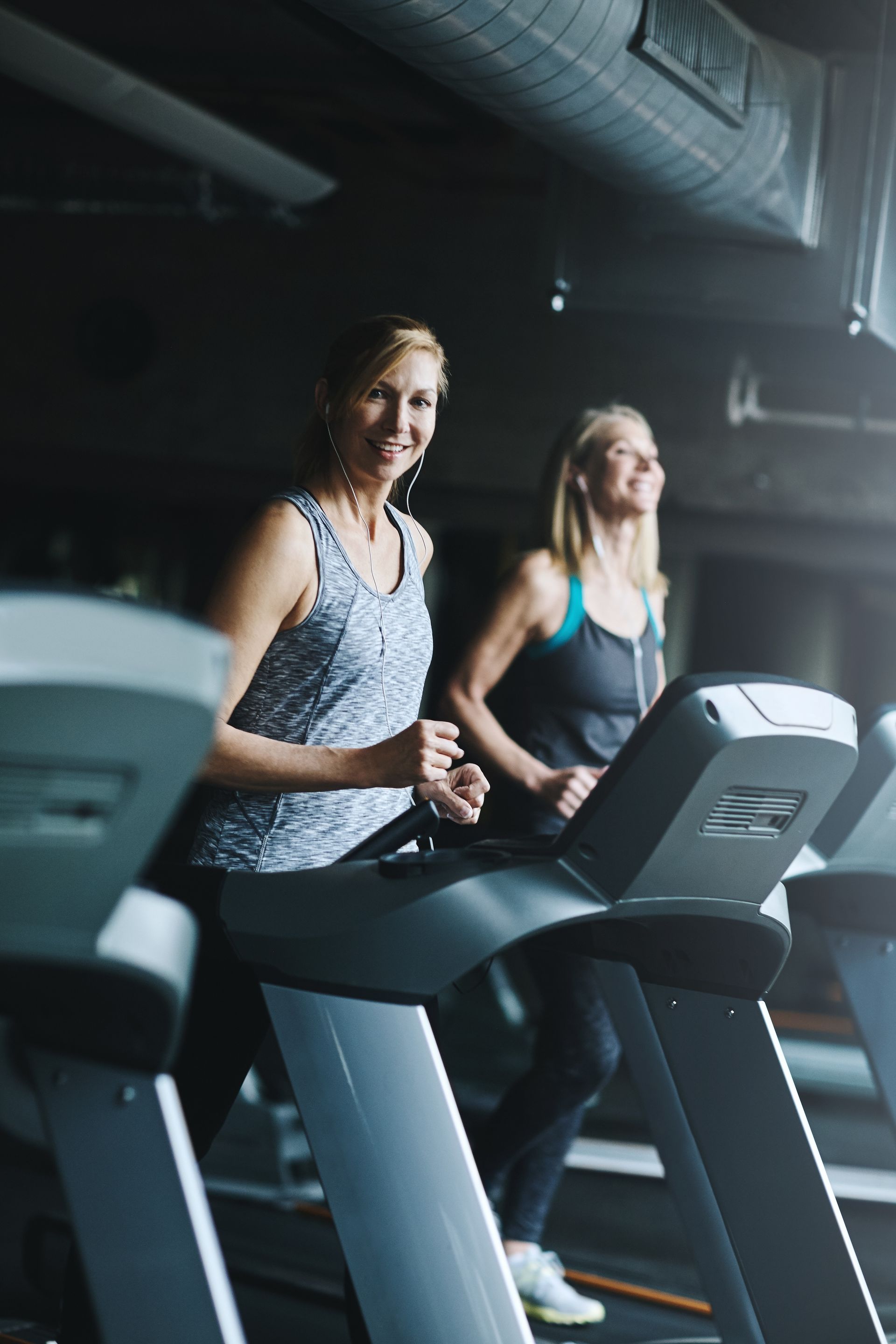 Two women running on treadmills in a dimly lit gym