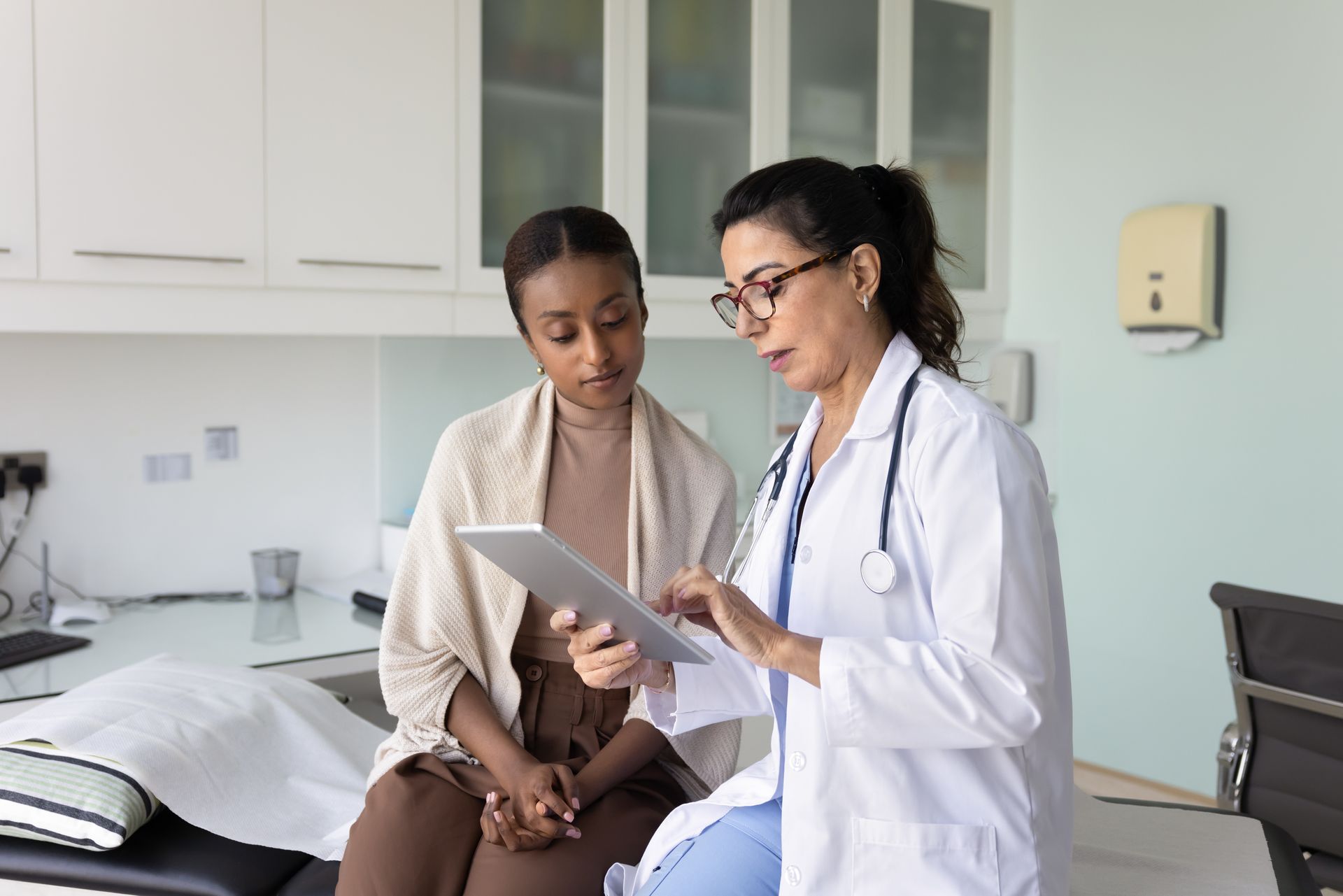 Doctor reviewing a tablet with a seated patient in a clinic exam room