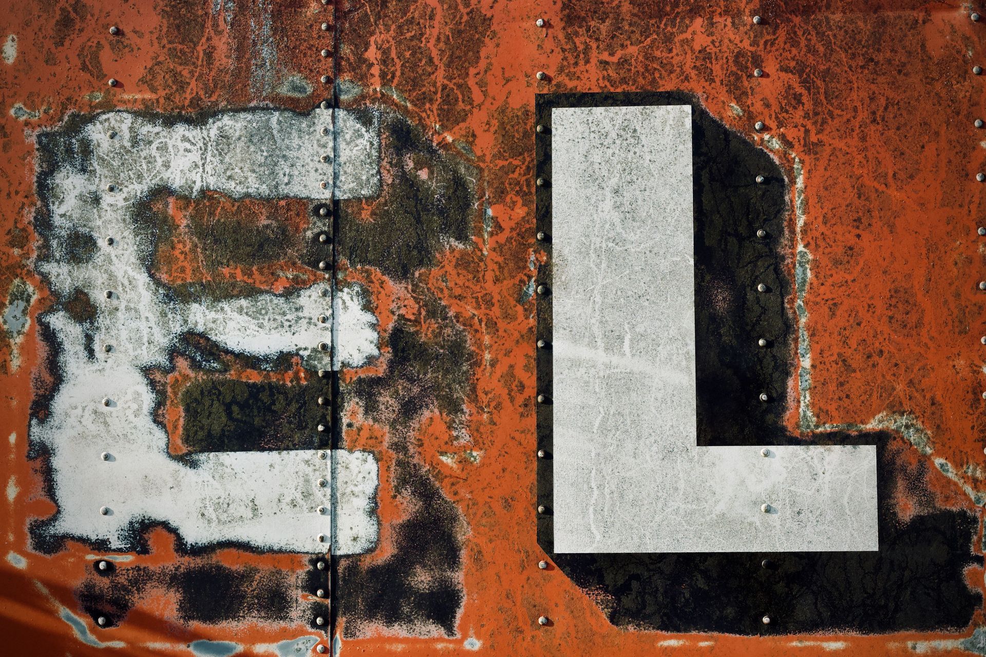 Verwitterte weiße Buchstaben „EL“ auf einer orangefarbenen, rostigen Metalloberfläche