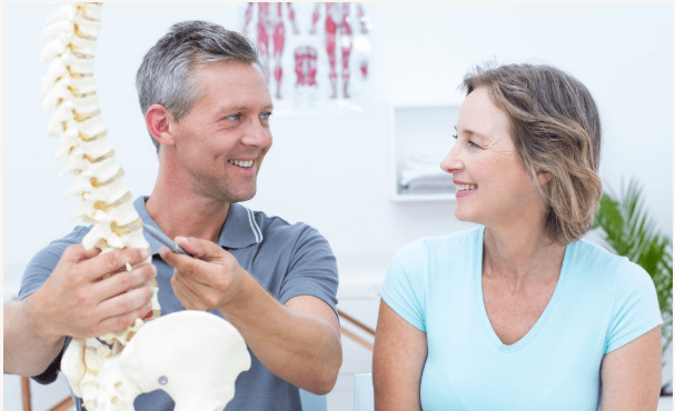 A man and a woman are looking at a model of a spine.