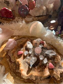 There are many different types of crystals on the table. Close-up of various crystals on a rustic wooden base, including pink and clear stones with a fluffy white backdrop.