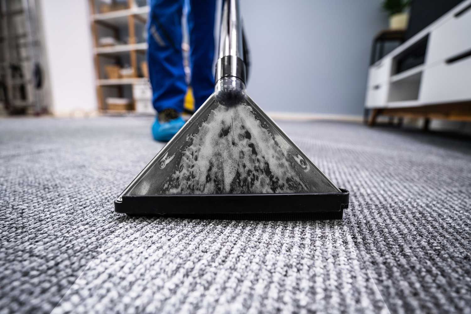 A professional cleaner using a carpet extraction machine on a textured gray carpet.