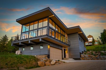 Modern house with large glass balcony at sunset, surrounded by rocks and trees