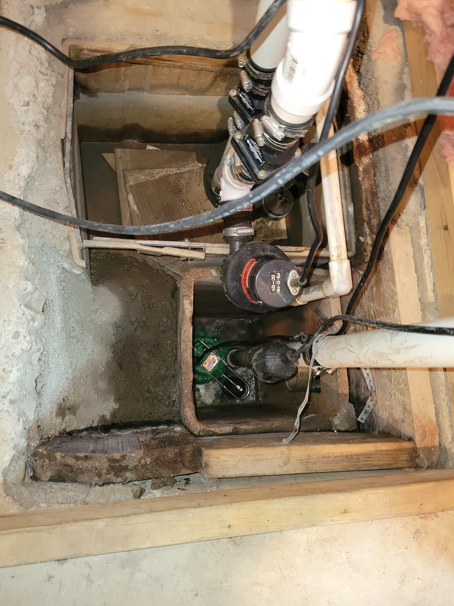 a drain in a basement with pipes and wires coming out of it .