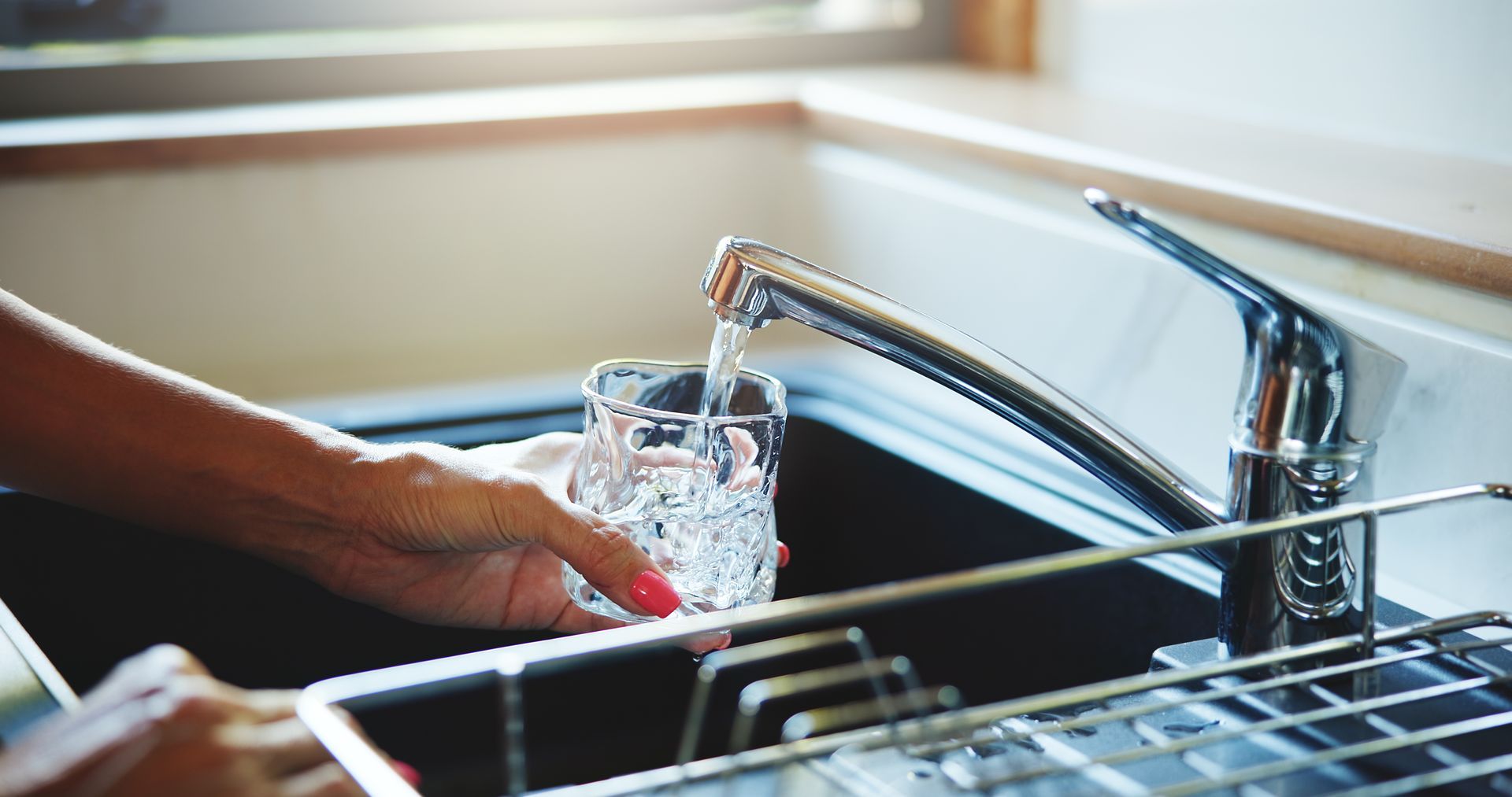 Hand holding glass under running faucet in kitchen sink.
