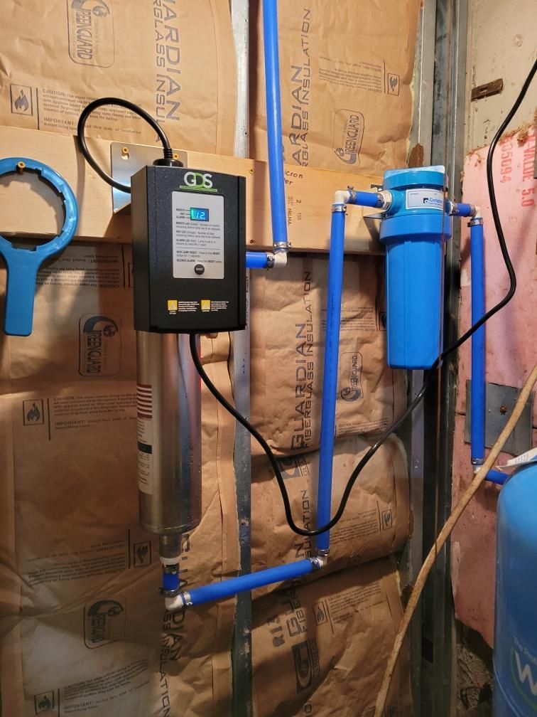 Water filtration system with blue pipes, filters, and a control box installed on a wall.