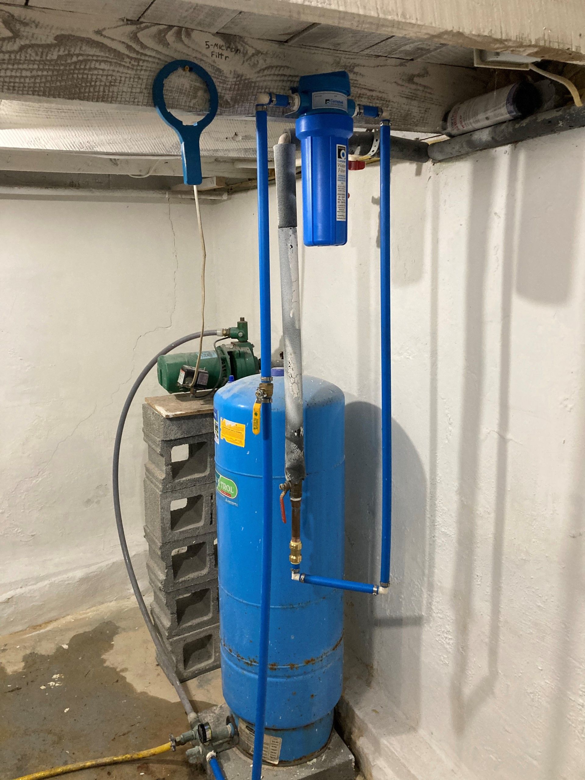 Blue water well pressure tank with connected pipes and filter in a basement.