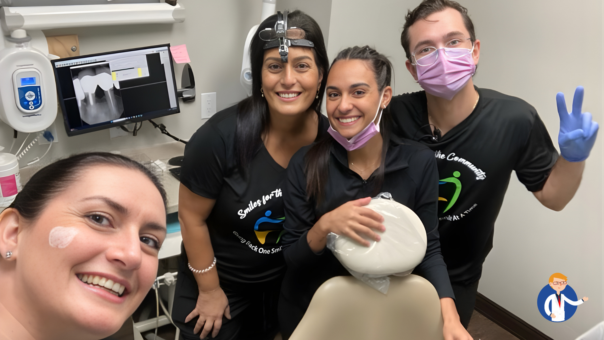 Four people in a dental office. Patient smiles with staff; one wears a surgical mask and gloves, all in matching shirts.